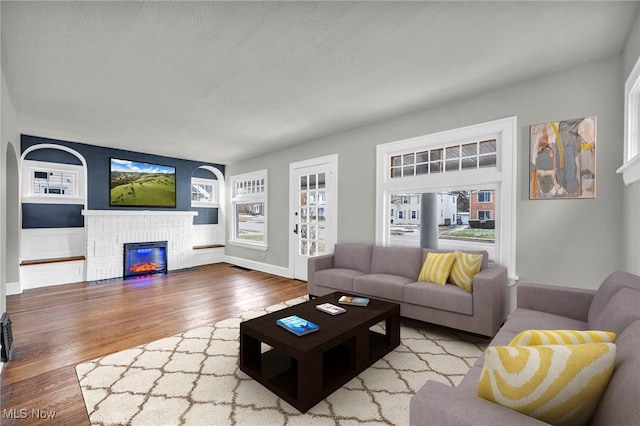 living area with baseboards, built in shelves, wood finished floors, a textured ceiling, and a fireplace