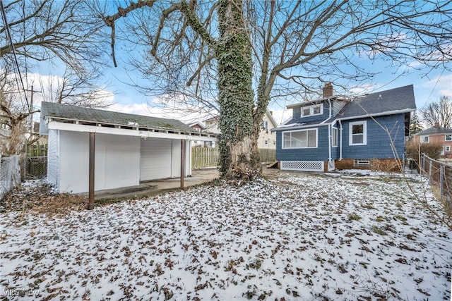 snow covered back of property with an outbuilding, a fenced backyard, and a chimney