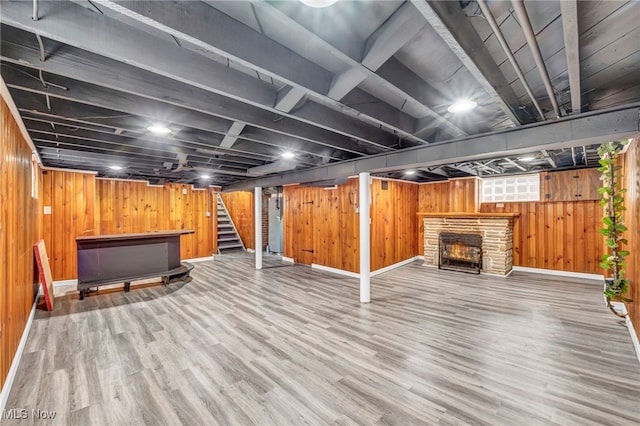 finished below grade area featuring stairway, wooden walls, a stone fireplace, wood finished floors, and baseboards