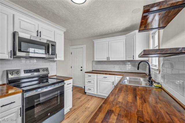 kitchen featuring wood counters, stainless steel appliances, light wood-style floors, white cabinetry, and a sink