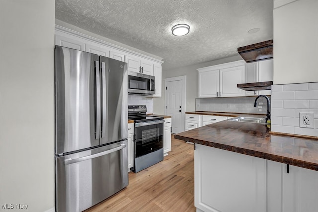 kitchen with wood counters, stainless steel appliances, light wood-type flooring, white cabinetry, and a sink