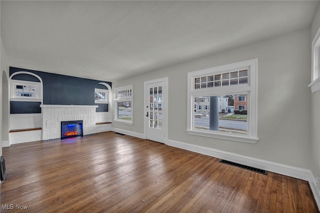 unfurnished living room featuring a brick fireplace, wood-type flooring, visible vents, and a healthy amount of sunlight