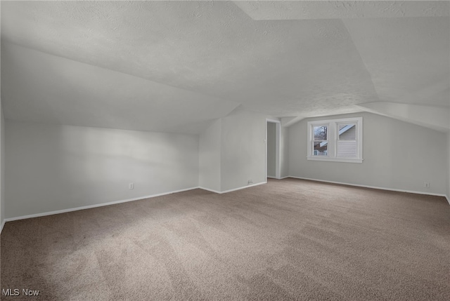 additional living space with baseboards, vaulted ceiling, a textured ceiling, and carpet flooring