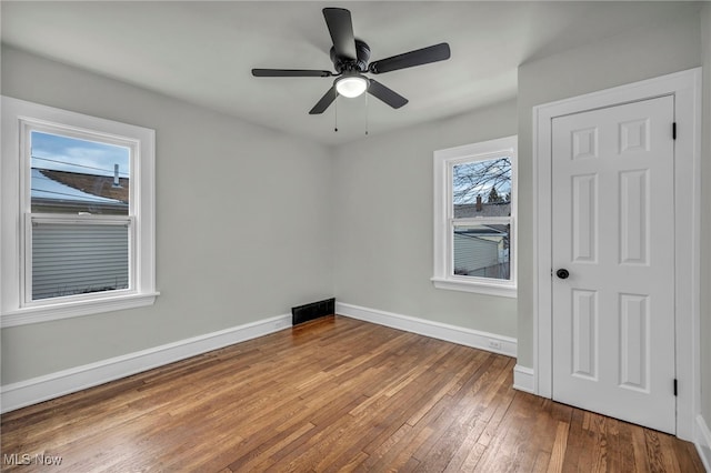 empty room featuring wood-type flooring, visible vents, baseboards, and a ceiling fan