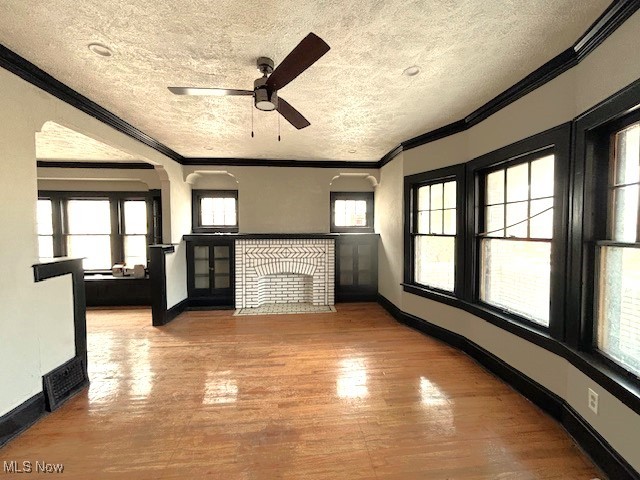 unfurnished living room featuring baseboards, a textured ceiling, ornamental molding, and wood finished floors