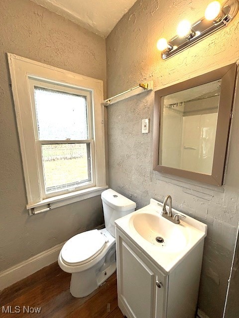 bathroom featuring a textured wall, toilet, wood finished floors, vanity, and baseboards