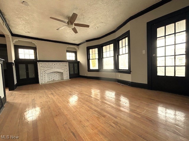 unfurnished living room featuring ornamental molding, wood-type flooring, a healthy amount of sunlight, and a fireplace