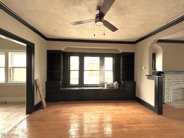 unfurnished room with baseboards, ceiling fan, wood finished floors, crown molding, and a textured ceiling