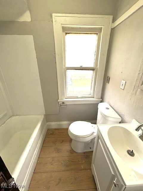 full bath featuring a tub to relax in, toilet, wood finished floors, vanity, and baseboards