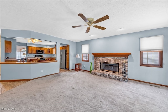 unfurnished living room featuring light colored carpet, a ceiling fan, a brick fireplace, a textured ceiling, and baseboards