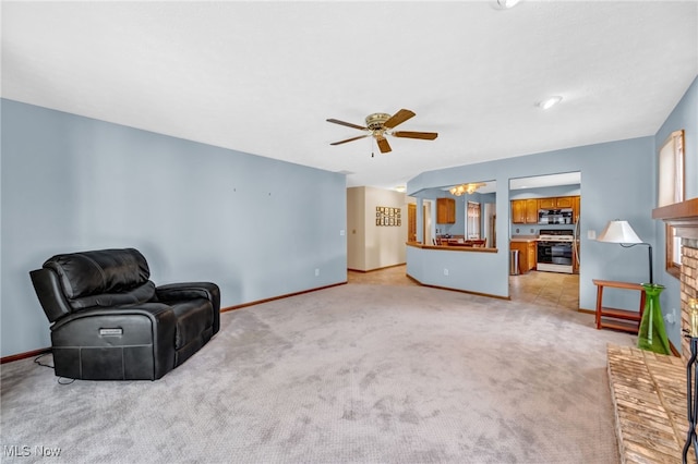 living area featuring light carpet, a brick fireplace, baseboards, and a ceiling fan