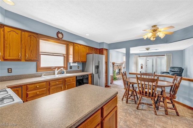 kitchen with black dishwasher, brown cabinets, a sink, a textured ceiling, and stainless steel fridge