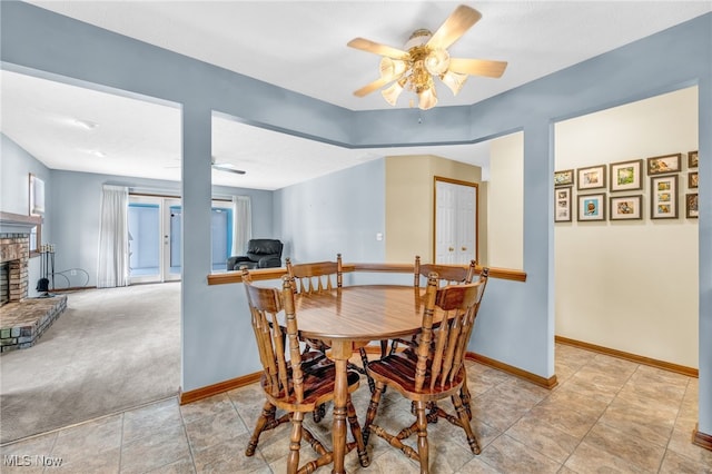 dining space featuring a brick fireplace, ceiling fan, baseboards, and light colored carpet