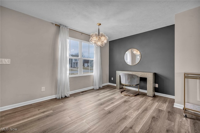 unfurnished living room with a chandelier, a textured ceiling, wood finished floors, and baseboards