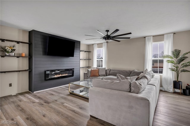 living room featuring a fireplace, a ceiling fan, and wood finished floors