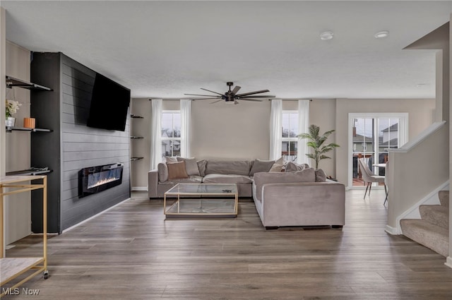 living room featuring baseboards, ceiling fan, wood finished floors, stairs, and a fireplace