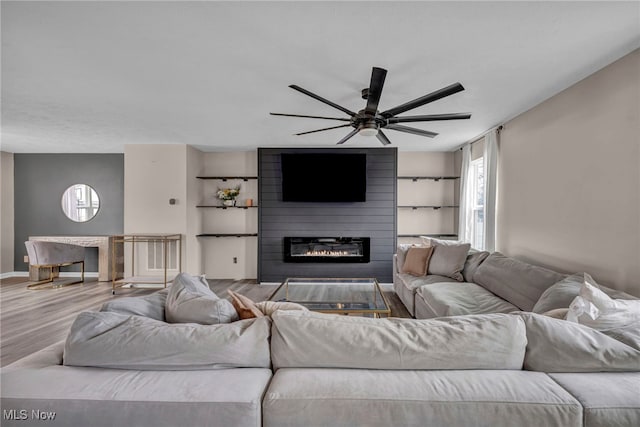 living area with a large fireplace, ceiling fan, baseboards, and wood finished floors