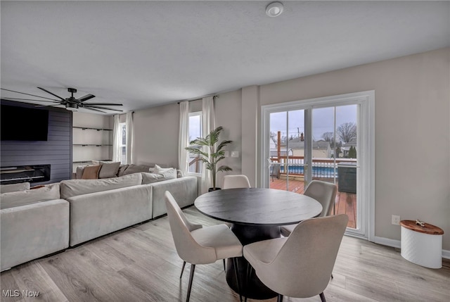 dining space with light wood-type flooring, ceiling fan, a fireplace, and baseboards