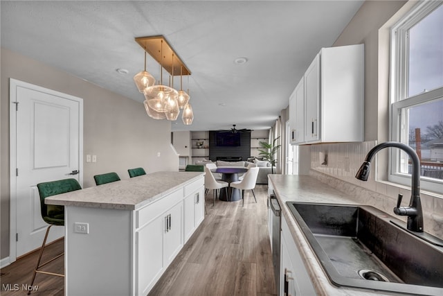 kitchen featuring wood finished floors, a kitchen island, a sink, and white cabinets