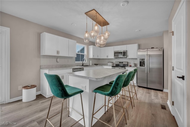 kitchen with a breakfast bar, stainless steel appliances, light countertops, a sink, and light wood-type flooring