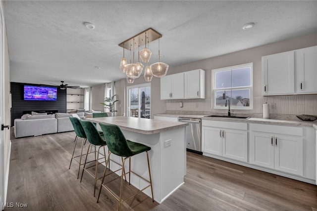 kitchen with dishwasher, wood finished floors, a center island, light countertops, and a sink