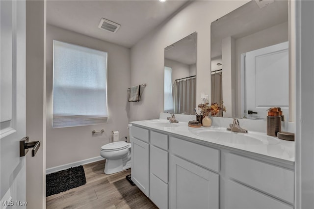 bathroom with toilet, a sink, visible vents, and wood finished floors