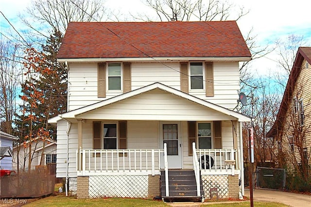 american foursquare style home featuring covered porch, roof with shingles, and a front lawn