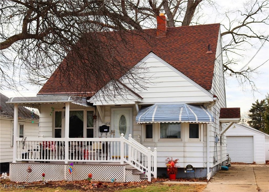 view of front of property featuring a detached garage, a chimney, a shingled roof, covered porch, and an outdoor structure