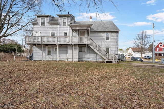 back of property with a deck, a chimney, stairs, and a lawn