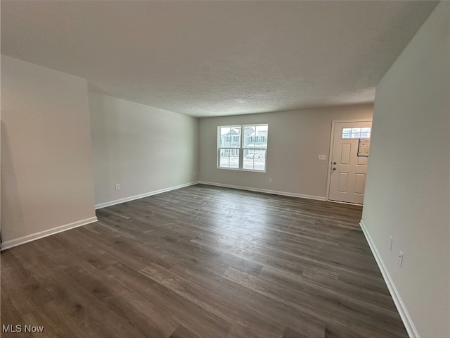 unfurnished living room featuring a textured ceiling, dark wood finished floors, and baseboards