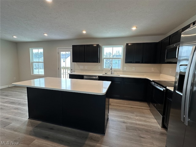 kitchen featuring stainless steel appliances, a sink, light wood-style flooring, and dark cabinets