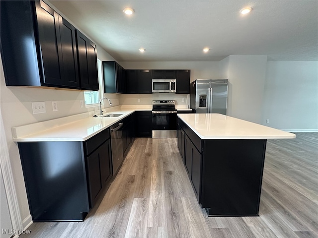 kitchen featuring a kitchen island, a sink, appliances with stainless steel finishes, dark cabinetry, and light wood-type flooring