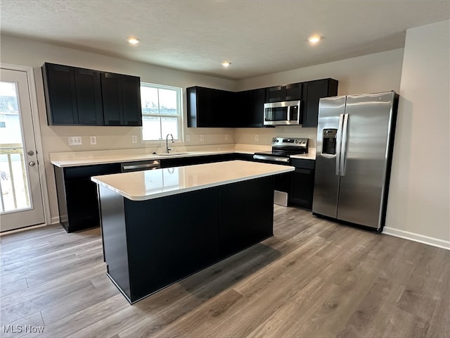 kitchen with light wood-style flooring, a sink, light countertops, appliances with stainless steel finishes, and dark cabinetry