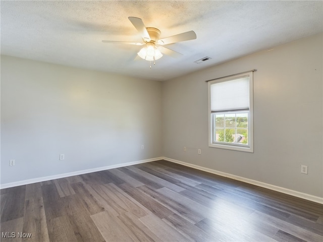 empty room with a textured ceiling, dark wood-type flooring, visible vents, and baseboards