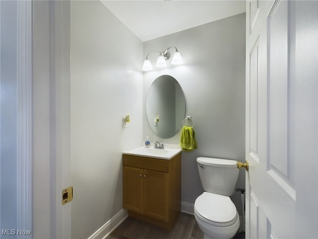 half bath with baseboards, vanity, toilet, and wood finished floors