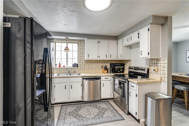 kitchen featuring tasteful backsplash, appliances with stainless steel finishes, light countertops, white cabinetry, and a sink