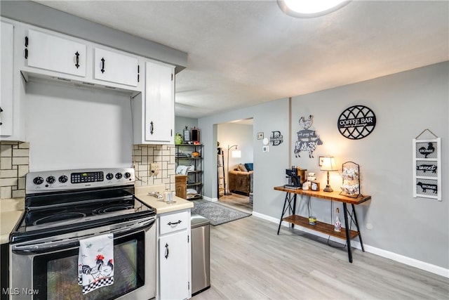 kitchen with light countertops, light wood-style flooring, electric range, decorative backsplash, and white cabinetry