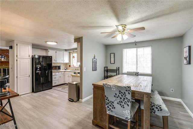 kitchen with plenty of natural light, stainless steel microwave, white cabinets, and black fridge with ice dispenser