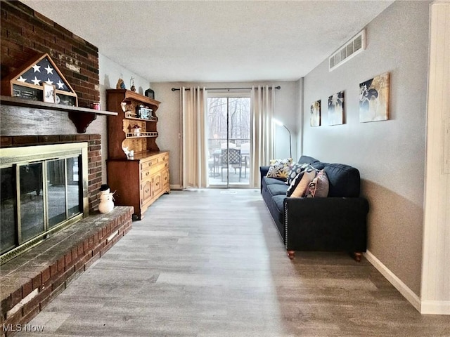 living area featuring light wood-style flooring, a brick fireplace, visible vents, and baseboards