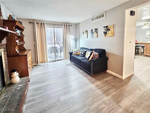 living area featuring a brick fireplace, baseboards, visible vents, and wood finished floors