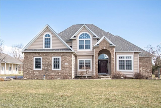 view of front of home featuring a shingled roof, a front lawn, and brick siding