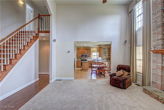 sitting room featuring baseboards, a high ceiling, stairs, and light colored carpet