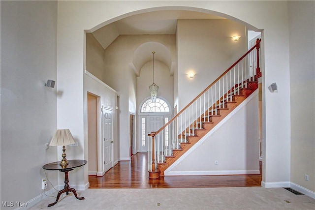 entrance foyer with visible vents, a towering ceiling, stairs, baseboards, and carpet