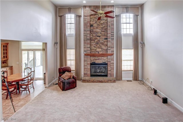 carpeted living room featuring plenty of natural light, a stone fireplace, a high ceiling, and ceiling fan