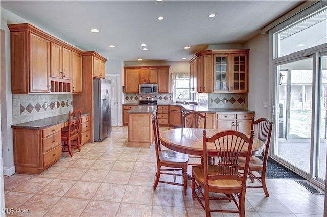 kitchen featuring stainless steel appliances, a sink, visible vents, brown cabinetry, and glass insert cabinets