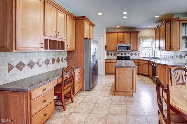 kitchen featuring a kitchen island, appliances with stainless steel finishes, brown cabinets, dark stone countertops, and built in desk