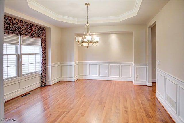 empty room featuring a chandelier, light wood-type flooring, a raised ceiling, and visible vents