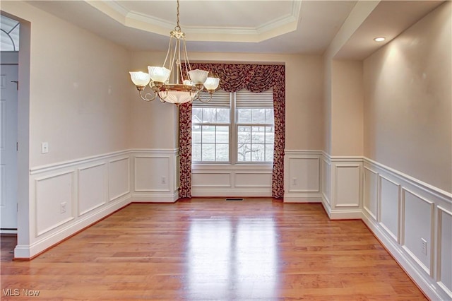 unfurnished dining area featuring a chandelier, a tray ceiling, visible vents, and light wood finished floors