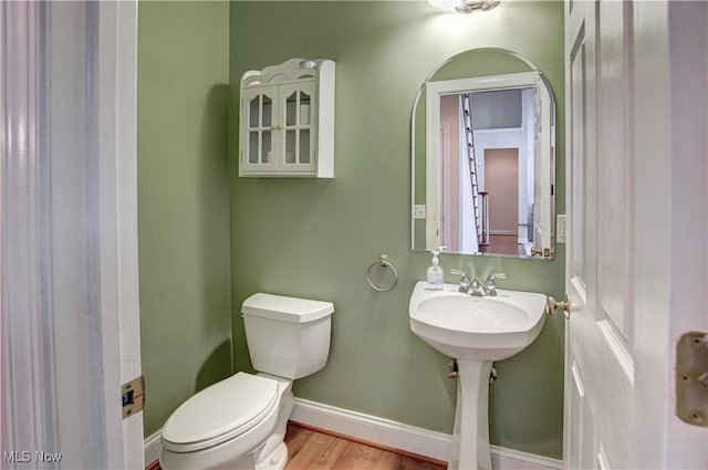 half bathroom with baseboards, a sink, toilet, and wood finished floors