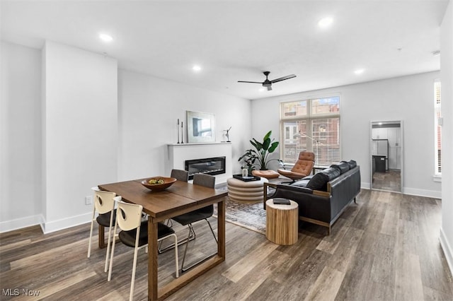 living area featuring baseboards, a glass covered fireplace, ceiling fan, wood finished floors, and recessed lighting